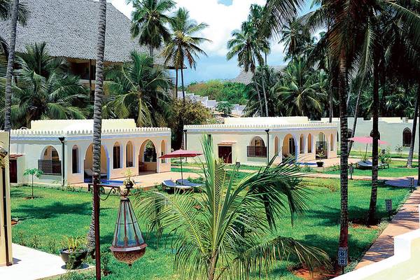 Außenansicht des Bahari Zanzibar Hotels mit Gebäuden, Palmen und Sonnenschirmen.