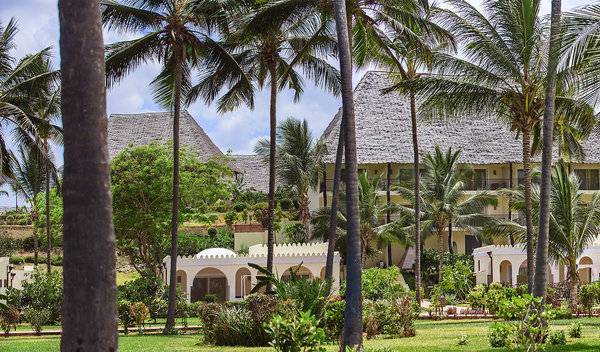 Außenansicht des Bahari Zanzibar Hotels mit traditionellen Dächern und tropischen Pflanzen.