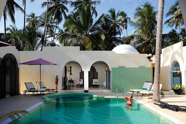 Außenpoolbereich des Bahari Zanzibar Hotels mit Sonnenschirm, Liegestühlen und Palmen.