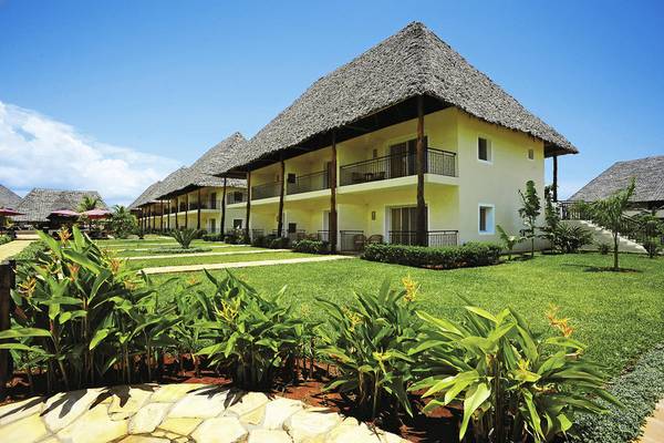 Außenansicht des Bahari Zanzibar Hotels mit gelben Gebäuden und Strohdächern auf einem grünen Rasen.