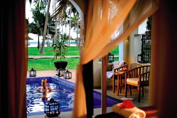 Eine Frau schwimmt im Pool des Bahari Zanzibar Hotels mit Blick auf die Außenterrasse.