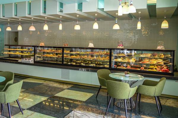 Innenansicht der Patisserie im Royal Wings Hotel mit Vitrinen voller Gebäck und grünen Stühlen.