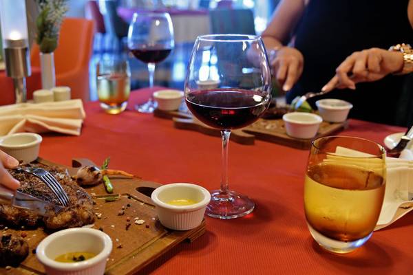 Personen essen am Tisch im Royal Wings Hotel mit Steak, Wein und Beilagen.
