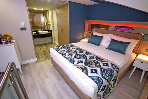 Innenansicht des Schlafzimmers im Royal Wings Hotel mit einem Bett, Kissen, Tisch und Badezimmerzugang.