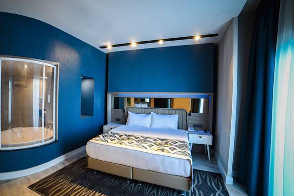 Ein blaues Hotelzimmer mit einem großen Fenster, das zu einer Badewanne führt, einem Bett und einem Nachttisch.