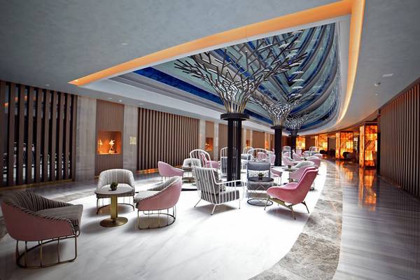 Innenansicht der Lobby des Royal Wings Hotels mit runden Tischen und Stühlen, hohen Säulen und einer gemusterten Decke.