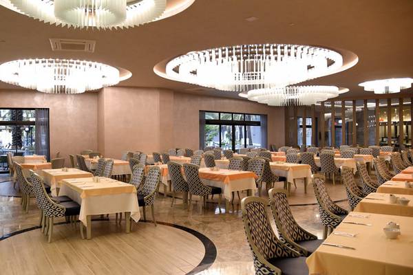 Foyer-Bereich des Royal Wings Hotels mit runden Tischen, Stühlen und großen Kronleuchtern.