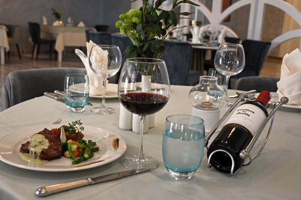 Ein Tisch im Royal Wings Hotel Restaurant mit einem Gericht, Weinglas und Wasserflasche.