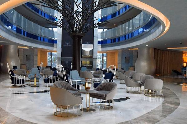 Lobby des Royal Wings Hotels mit modernen Möbeln und einer zentralen Baumskulptur.
