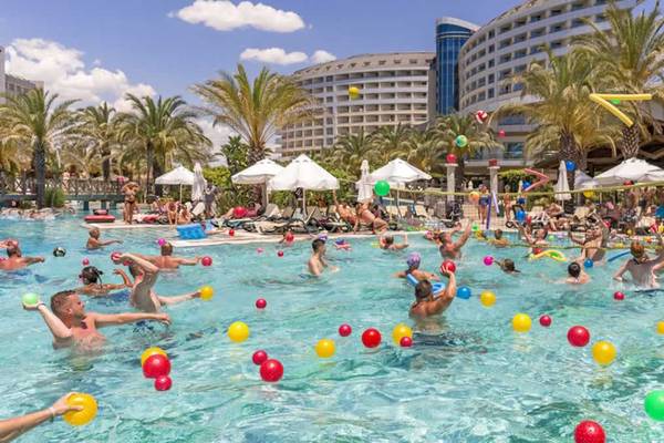 Gäste spielen Volleyball im Pool des Royal Wings Hotels mit vielen bunten Bällen.