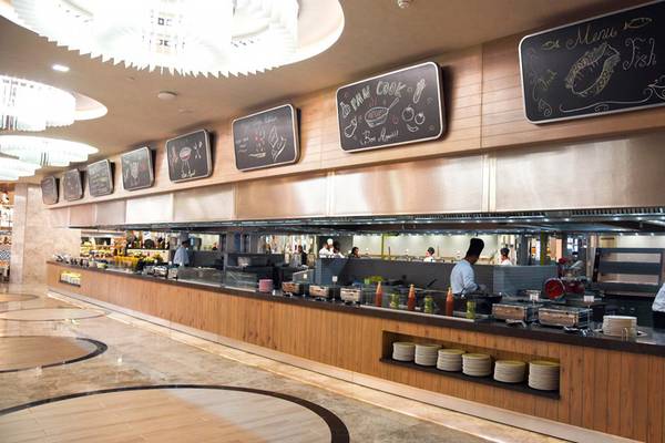 Innenansicht des Restaurants im Royal Wings Hotel mit Buffet und Köchen, die Gerichte zubereiten.