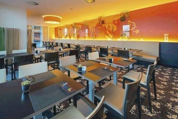 Innenansicht des Restaurants im Mövenpick Amsterdam City Centre Hotel mit gefüllten Tischen und Stühle.