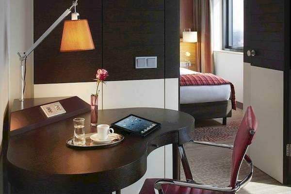 Hotelzimmer im Mövenpick Amsterdam City Centre mit Schreibtisch, Tablet, Tasse und Rose.