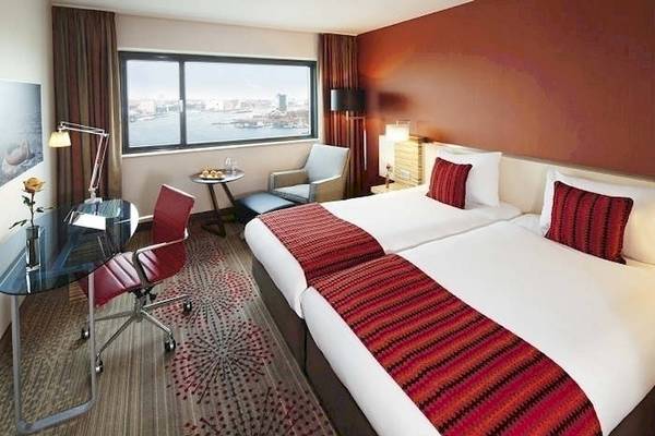 Hotelzimmer im Mövenpick Amsterdam City Centre mit zwei Betten, Schreibtisch und Stadtblick.