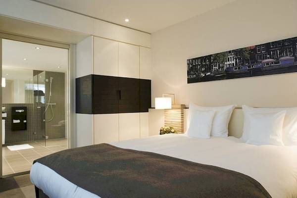 Hotelzimmer im Mövenpick Amsterdam City Centre mit Bett, Lampen und Panoramafenster.