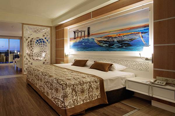 Innenansicht des Crystal Sunset Luxury Resort & Spa Hotelzimmers mit einem großen Bett, Nachttischen und einem Ausblick auf den Hafen.
