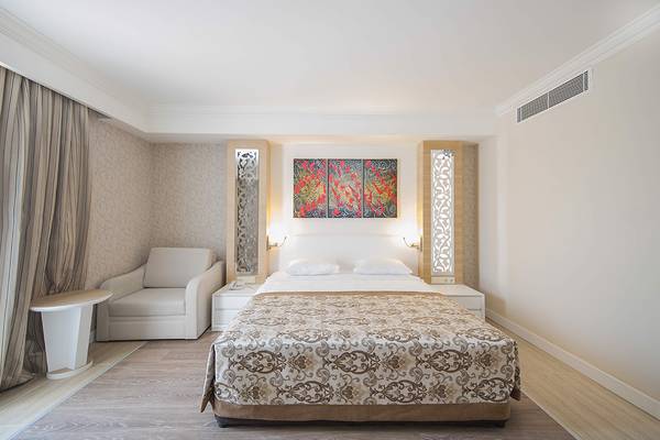 Schlafzimmer im Crystal Sunset Luxury Resort & Spa mit einem großen Bett, zwei Nachttischen und einer Wand mit drei Gemälden.