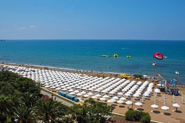 Luftaufnahme des Crystal Sunset Luxury Resort & Spa Strandes mit vielen Sonnenschirmen und Wassersportgeräten