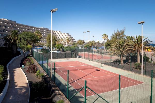 Tennisplatz im Freien am Grand Teguise Playa Hotel mit umzäuntem Spielfeld und umliegenden Palmen.
