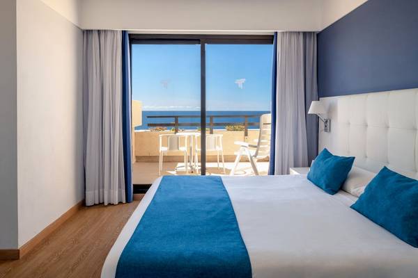 Zimmer im Grand Teguise Playa mit Blick auf das Meer und einen Balkon mit Tisch und Stühlen.