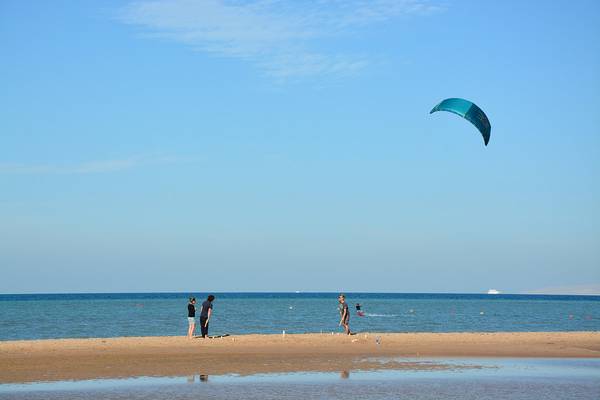 Drei Personen stehen am Strand, während ein Kitesurfer im Wasser ist.