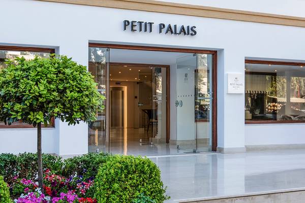 Die Vorderansicht des Petit Palais Hotels mit Eingangsbereich und Blumenbeeten davor.