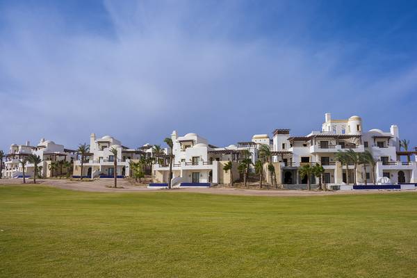 Reihe von weißen Gebäuden des Ancient Sands Golf Resorts mit blauem Rasen im Vordergrund.