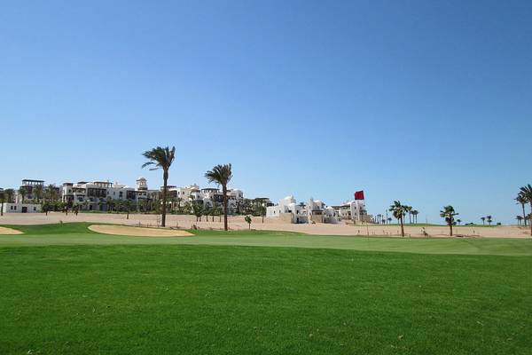Landschaftsansicht des Ancient Sands Golf Resorts mit grünem Rasen und Gebäuden im Hintergrund.