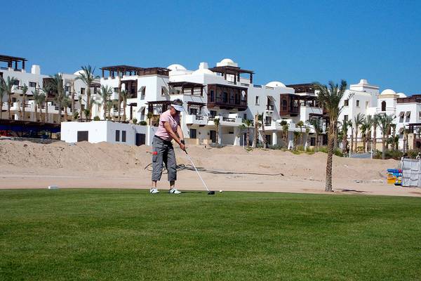 Golfspieler im Ancient Sands Golf Resort vor weißen Gebäuden und Palmen