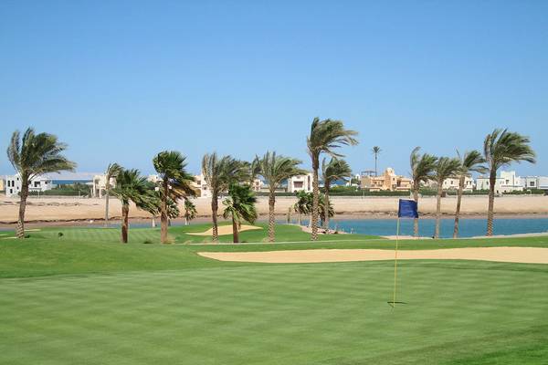 Golfplatz im Ancient Sands Golf Resort mit Palmen und Wasserhindernis.