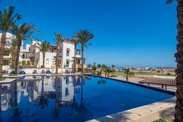 Außenpool des Ancient Sands Golf Resorts mit Palmen und Gebäuden im Hintergrund