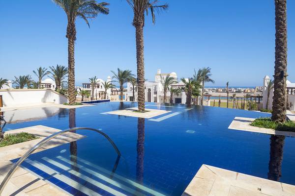 Außenpool des Ancient Sands Golf Resorts mit Palmen und Blick auf das Meer