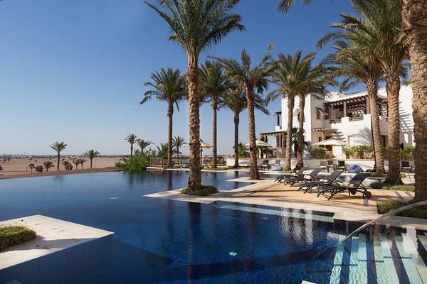 Ein Swimmingpool am Ancient Sands Golf Resort mit weißen Gebäuden und Palmen im Hintergrund.