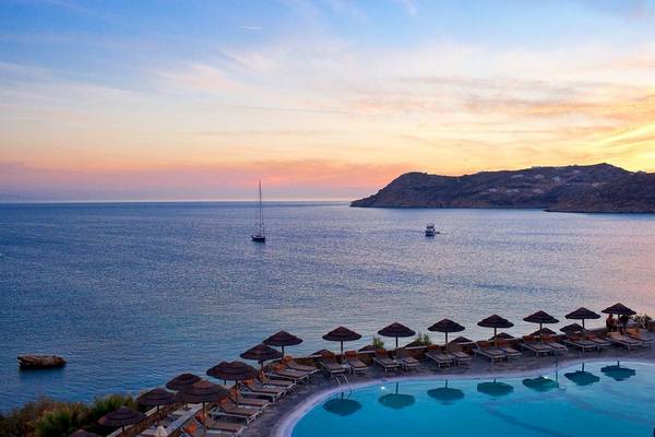 Aussicht auf das Meer vom Hotel Myconian Imperial mit Sonnenuntergang, Segelboot und Insel im Hintergrund.