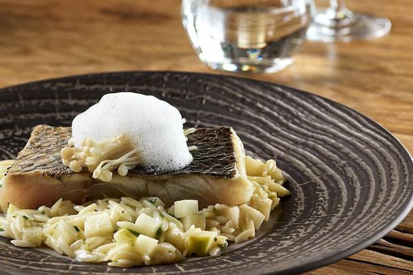 Fischgericht mit Reis und Gemüse auf einem schwarzen Teller auf einem Holztisch.