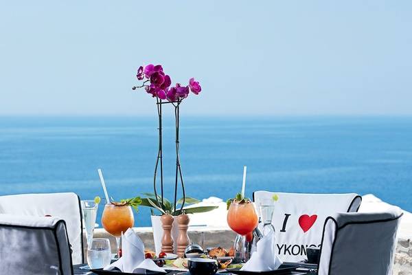 Terrasse des Myconian Imperial mit Blick auf das Meer und Getränken auf dem Tisch.