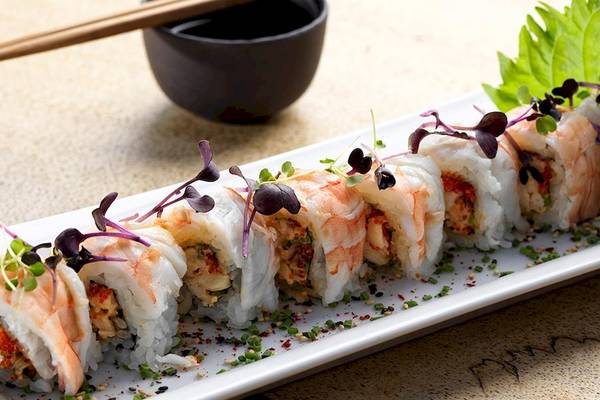 Ein Teller mit Sushi-Rollen, garniert mit kleinen Pflanzen, serviert mit Essstäbchen und einer Schüssel