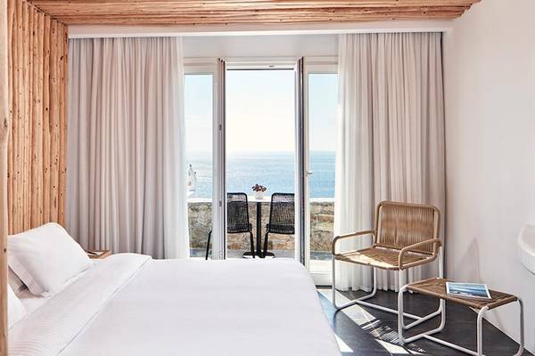 Zimmer im Myconian Imperial Hotel mit Blick auf das Meer und einer Terrasse mit Tisch und Stühlen.