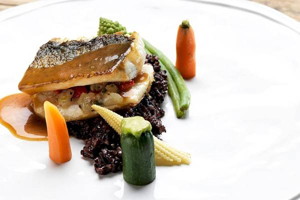 Ein Fischgericht auf einem weißen Teller, umgeben von gebratenem Reis und Gemüse.