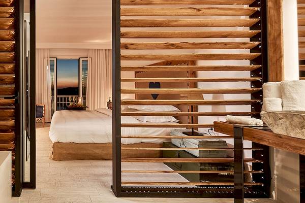 Schlafzimmer im Myconian Imperial mit zwei Betten, Holzwänden und Aussicht auf den Sonnenuntergang.