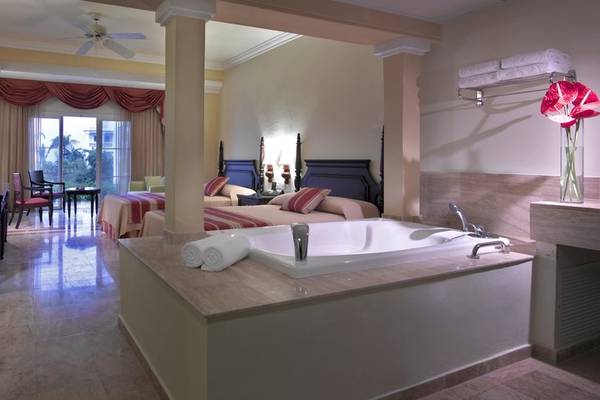 Suite im Grand Palladium Jamaica mit Badewanne, zwei Betten und Blick auf einen Balkon.