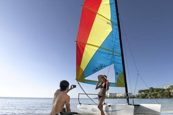 Paar am Strand mit einem bunten Katamaran-Segelboot, das die Frau abbremst.
