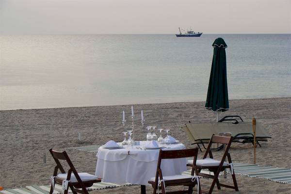 Ein Tisch auf dem Strand, geschmückt mit Kerzen und Geschirr, mit einem Boot im Hintergrund.