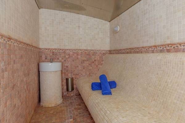 Saunabereich im Aparthotel Fontanellas Playa mit gefliesten Wänden, einer Bank, blauen Handtüchern und einem Waschbecken.