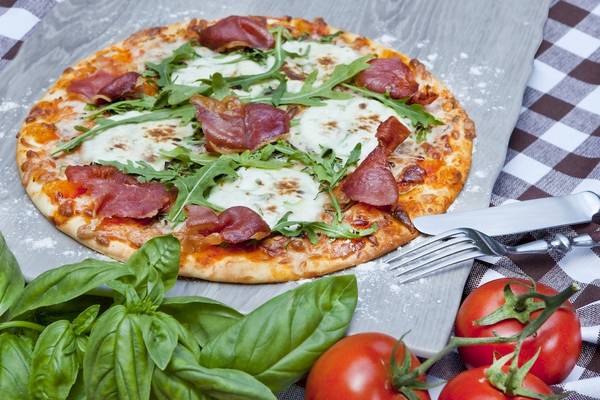 Eine Pizza mit Schinken, Rucola und Tomaten auf einem Marmorbrett.