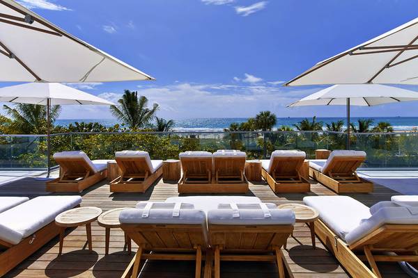 Terrasse des 1 Hotel South Beach mit mehreren Holzliegen und Sonnenschirmen, Blick auf den Ozean.