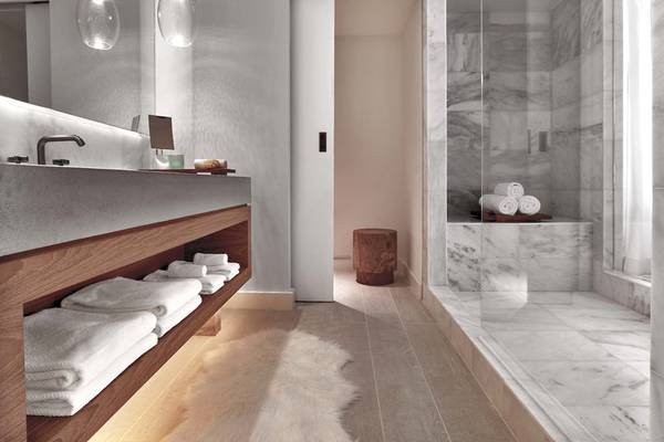 Innenansicht des Badezimmers im 1 Hotel South Beach mit Marmorfliesen, Glasdusche und Holzmöbeln.