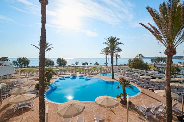 Außenbereich des Hipotels Flamenco mit Pool, Sonnenliegen und Sonnenschirmen am Meer