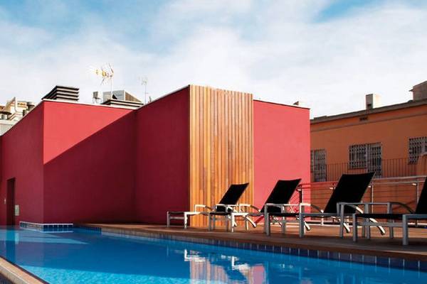 Pool auf der Dachterrasse des Barcelona Catedral Hotels mit roten Wänden und Lounge-Liegestühlen