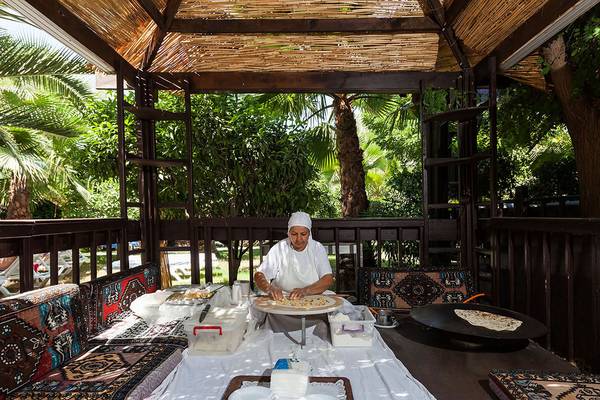 Frau in traditioneller Kleidung backt im Garten des Sultan of Side Hotels.